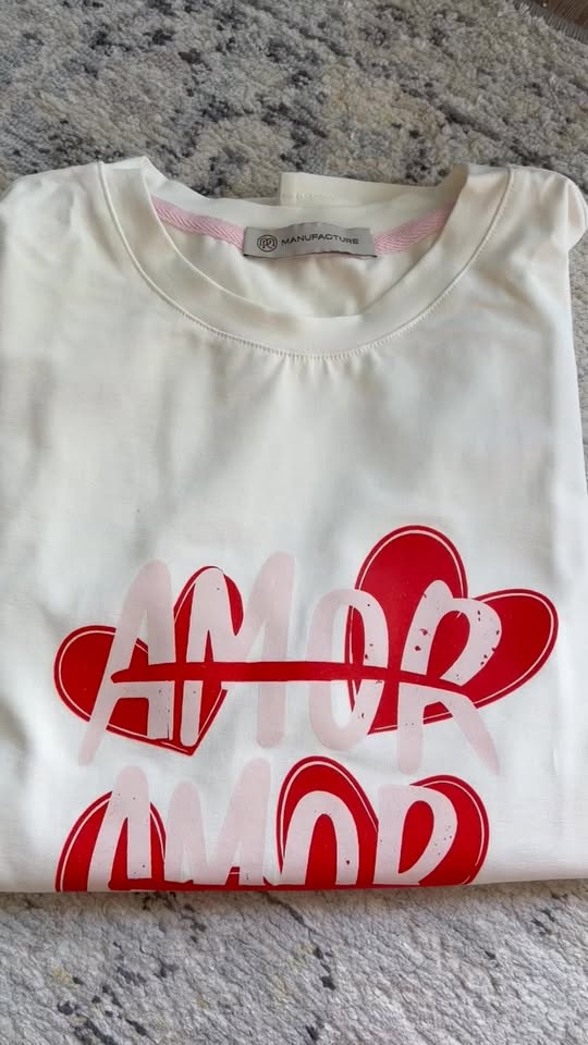 Cream t-shirt with a red and pink AMOR print, folded on a rug