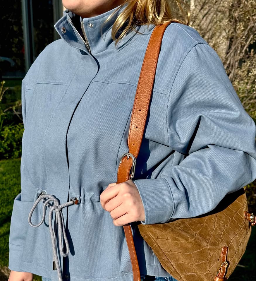 Mon Ami cotton bomber jacket in dusty blue with side drawstrings, worn with a tan crossbody bag