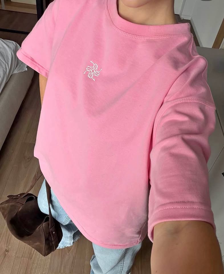 Pink cotton t-shirt with a small white embroidered emblem, worn with light jeans