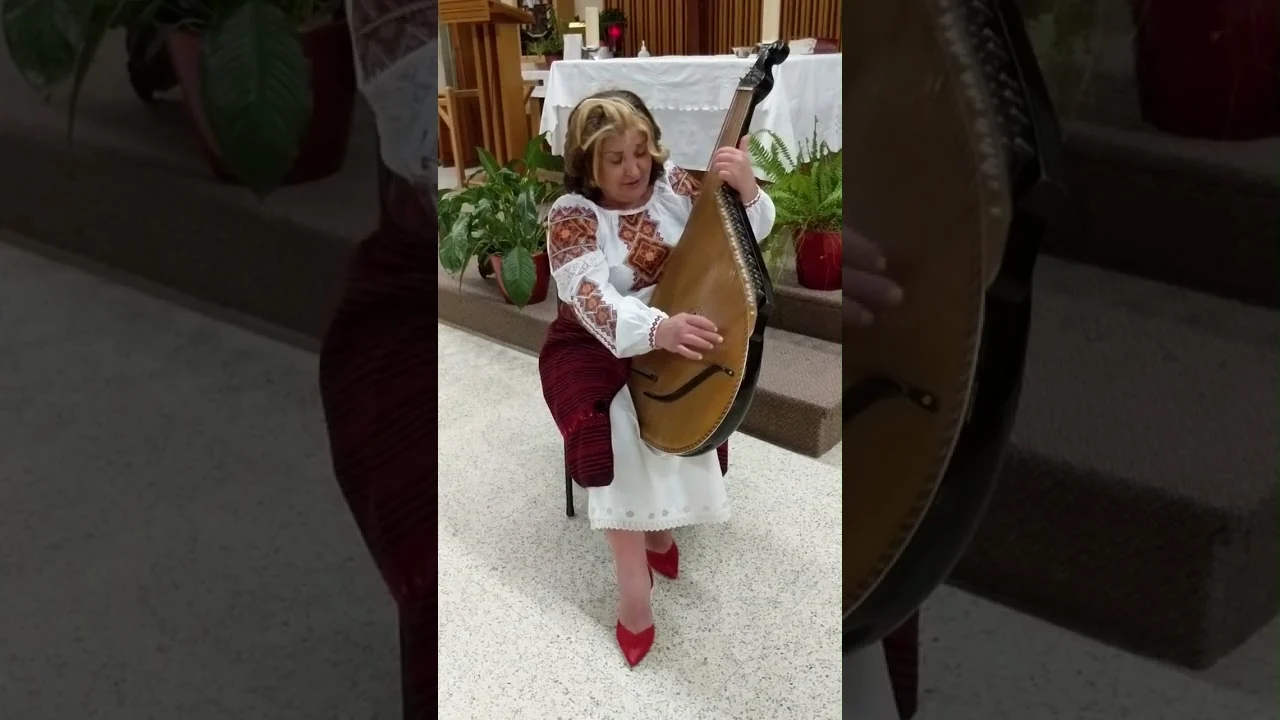 Tanya Navolska seated with her bandura in an embroidered blouse and burgundy wrap skirt, singing «Зоре моя вечірняя»