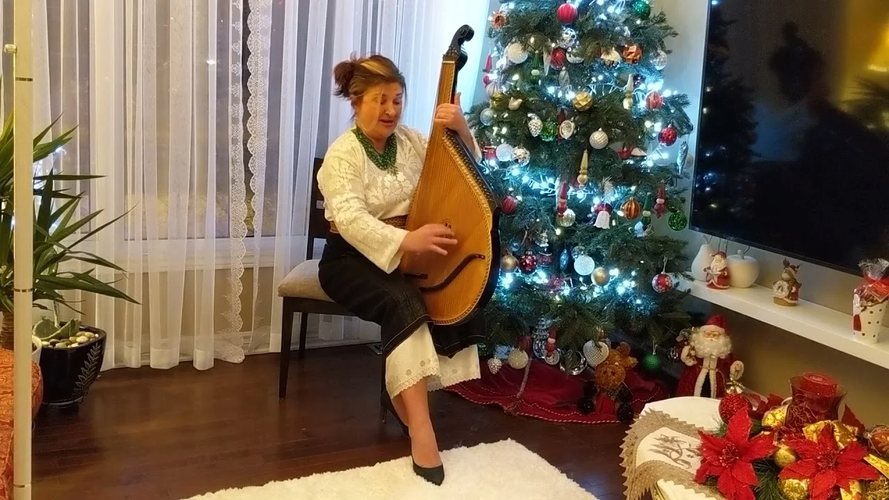 Tanya Navolska beside a Christmas tree with her bandura, singing the carol «По всьому світу стала новина»