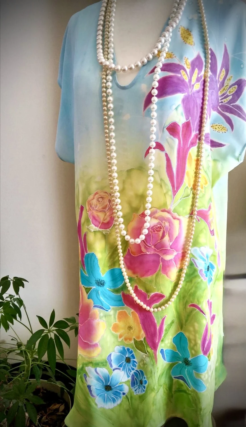 Hand-painted silk dress on a mannequin — roses and blue flowers on a green-to-blue ground, with pearl ropes