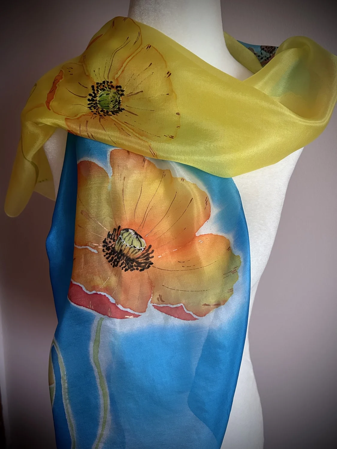 Hand-painted silk scarf on a mannequin — orange poppies on blue, with a yellow scarf draped over the shoulders