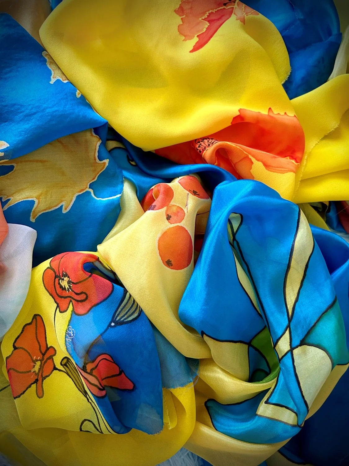 A heap of hand-painted silk scarves in blue and yellow with poppies and maple leaves