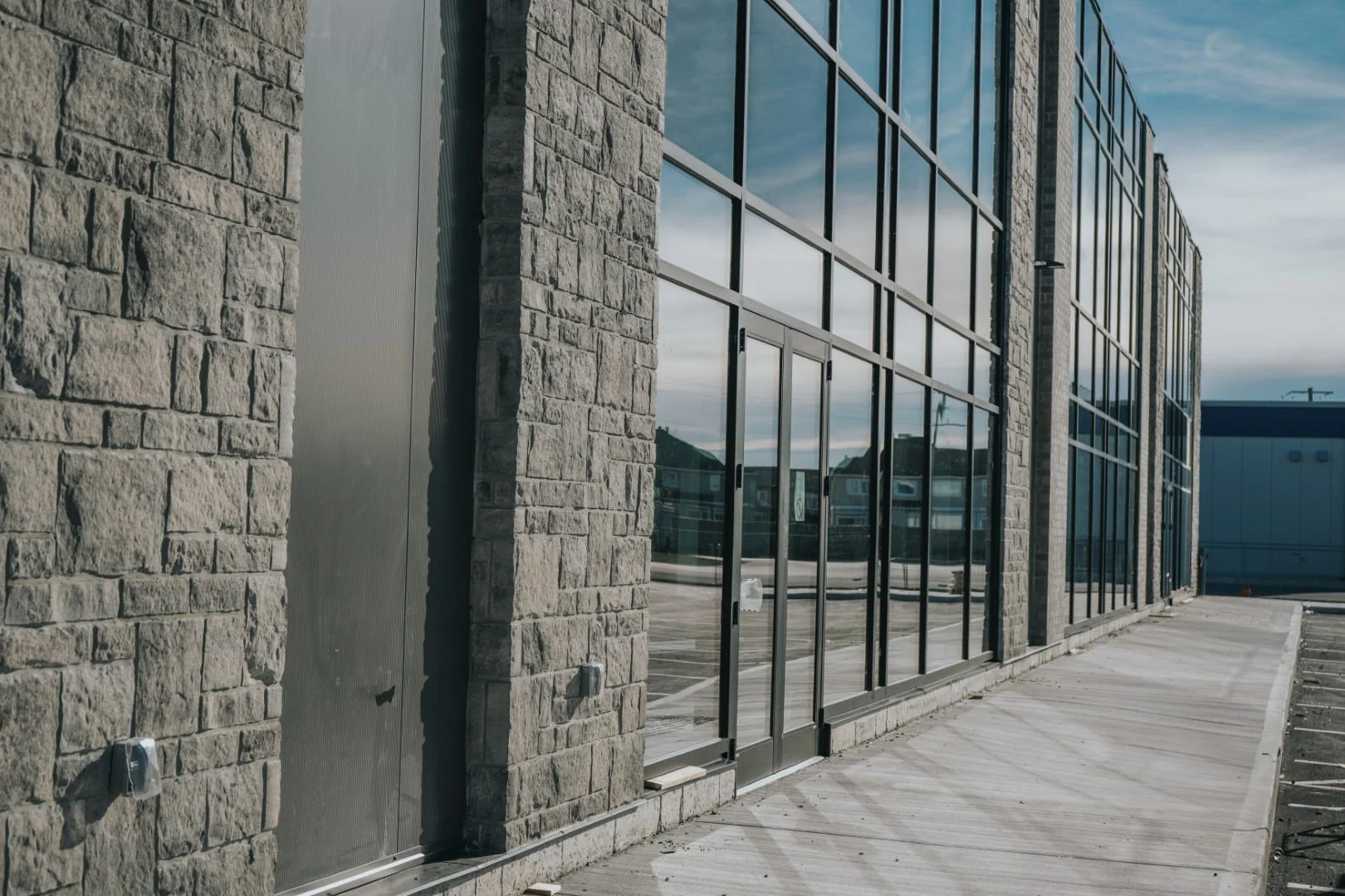 A newly finished commercial building with a stone facade and full-height glass storefront along a fresh concrete sidewalk