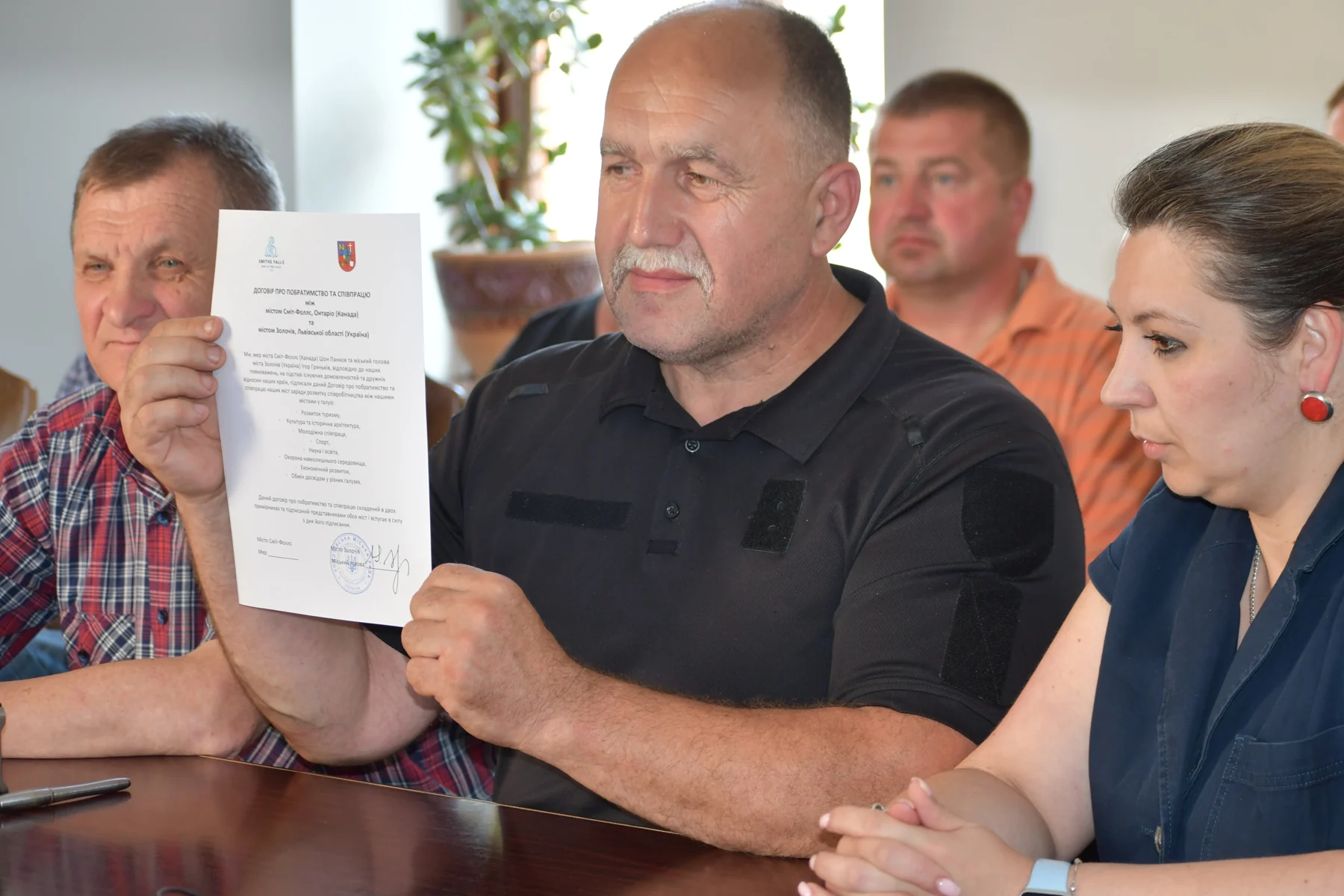 Mayor Ihor Hrynkiv of Zolochiv holding up the signed Ukrainian-language copy of the twinning agreement at a table with colleagues