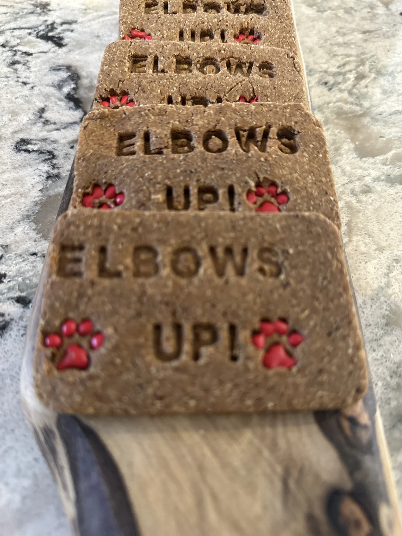 A row of large biscuits stamped "ELBOWS UP!" with red paw prints.