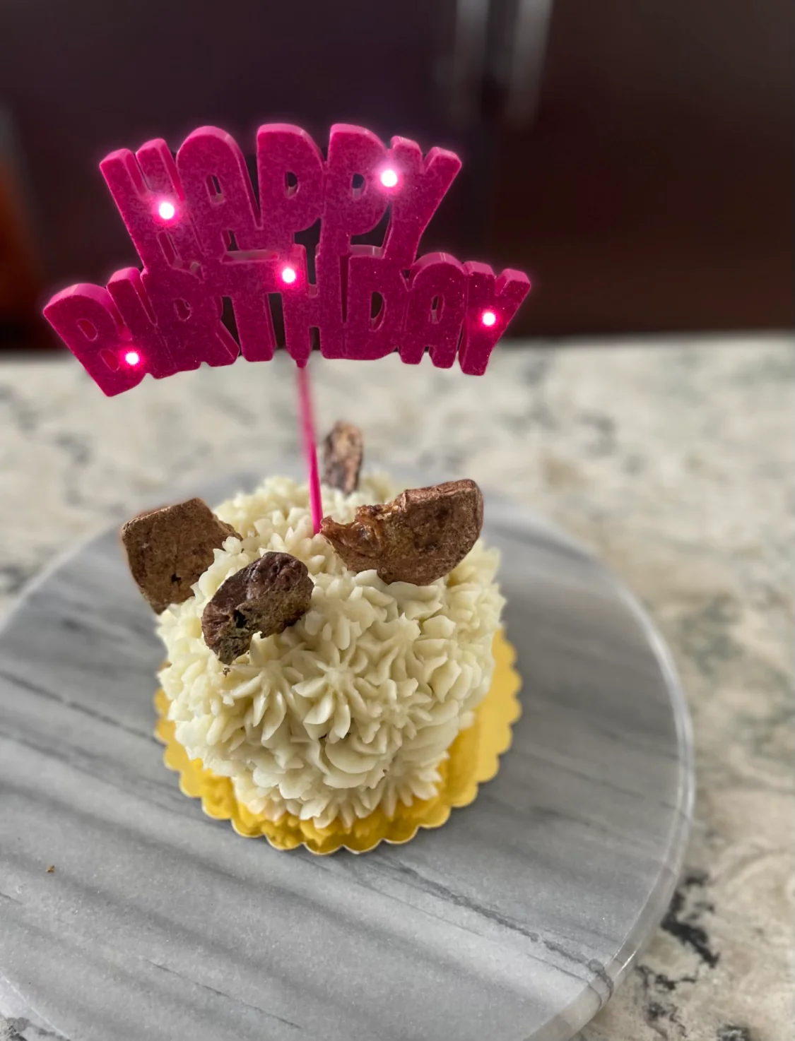 A small piped dog cake with a lit "Happy Birthday" topper.
